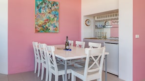 A dining area with a table and chairs, a bottle of champagne, and a colorful painting on the wall.