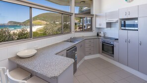 A modern kitchen with a large window overlooking a beach and hills.