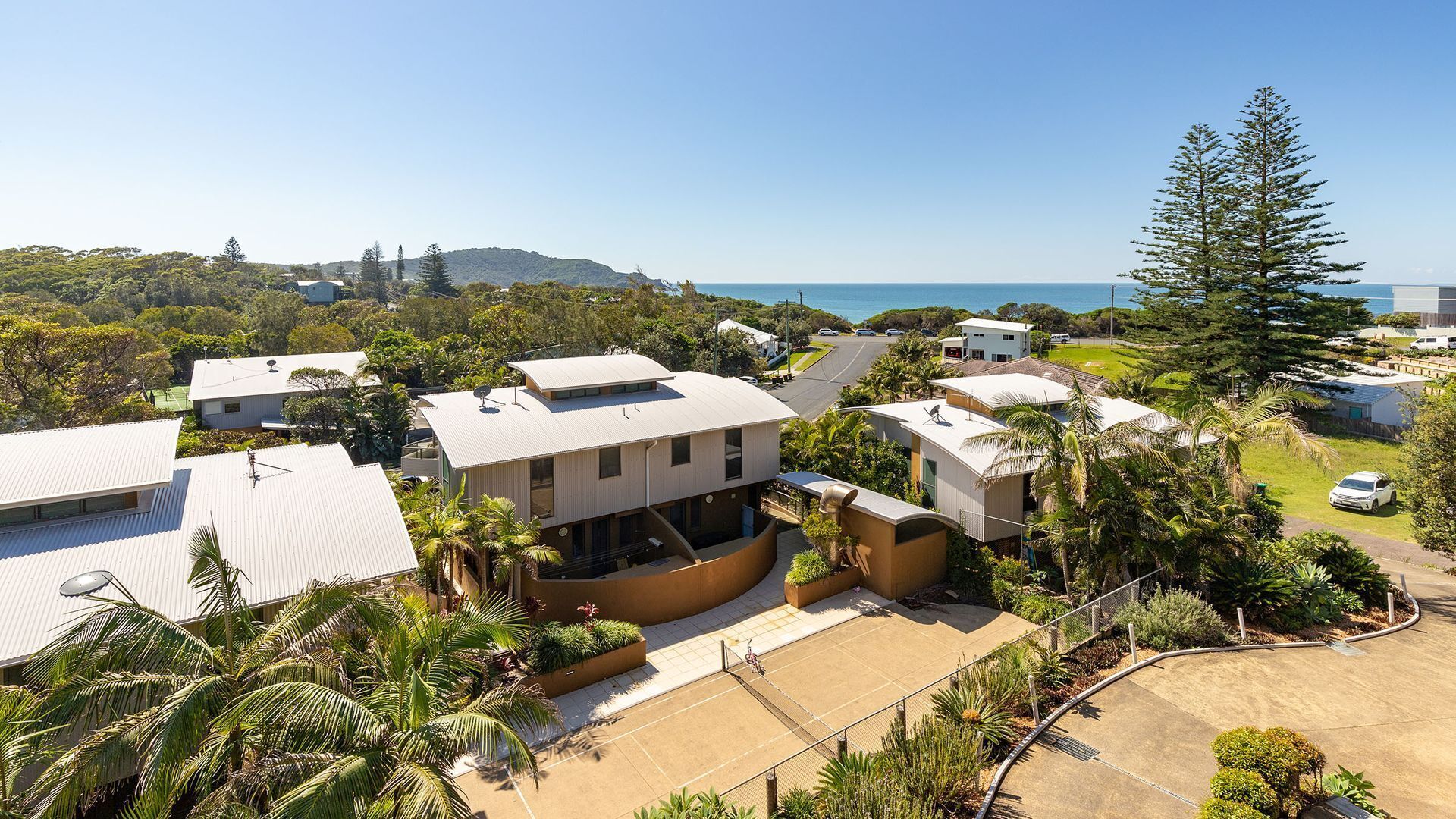 Un quartier résidentiel avec des maisons modernes, un court de tennis et une vue sur l’océan.