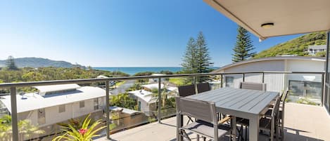 A balcony with a table and chairs, overlooking a coastal landscape with buildings and greenery.