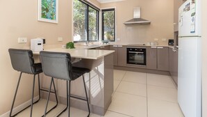 A modern kitchen with a central island, two bar stools, a built-in oven, and a refrigerator. - Boom 1 located just metres from Boomerang Beach one of the most beautiful beaches in Australia. (Boomerang Beach)
