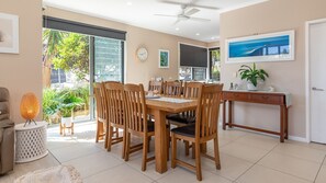 Un espace repas avec une table et des chaises en bois, un ventilateur de plafond et une vue sur la verdure à l’extérieur.