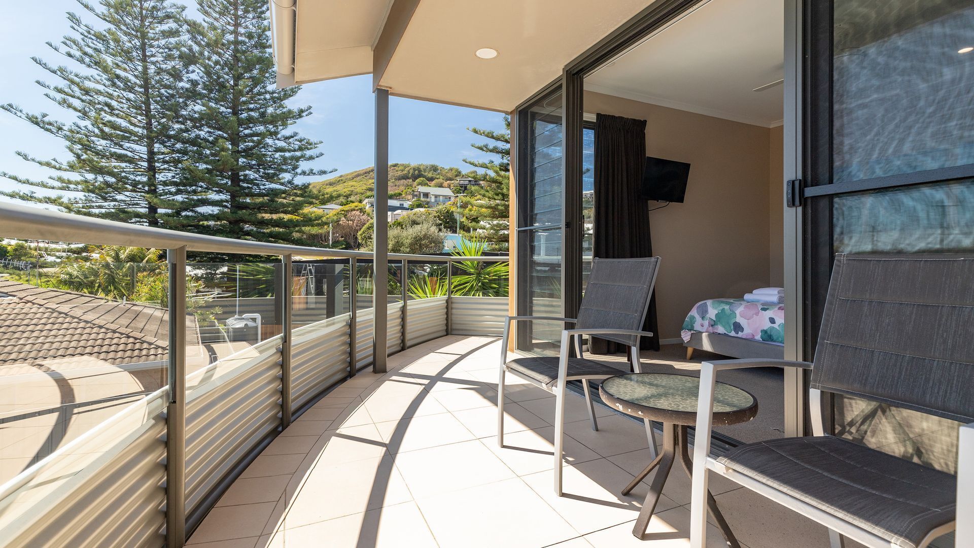 A balcony with a glass door, a bed, a TV, and a chair.