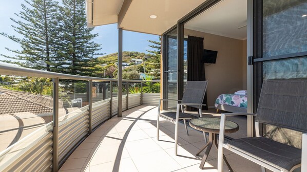 A balcony with a glass door, a bed, a TV, and a chair.