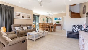 A spacious living room with a sofa, a dining table with chairs, and a staircase leading to an upper floor. - Boom 1 located just metres from Boomerang Beach one of the most beautiful beaches in Australia. (Boomerang Beach)