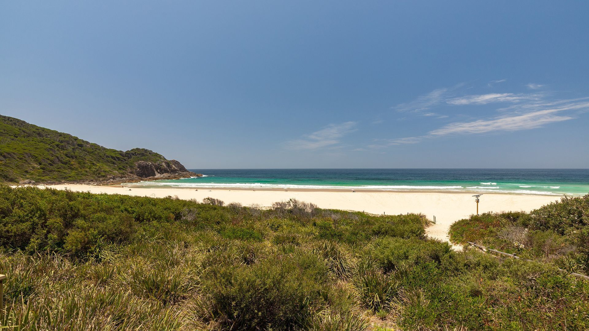 Een strand met helder turquoise water, een zandstrand en weelderige begroeiing.