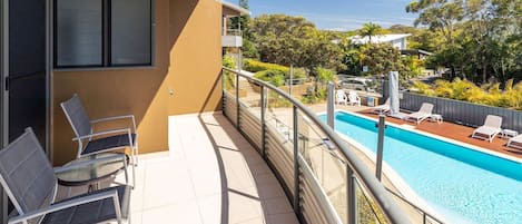 En balkong med en pool, stolar och utsikt över den omgivande grönskan.