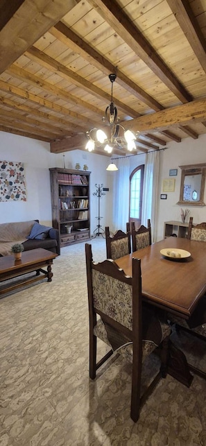 A dining area with a wooden table and chairs, a sofa, a bookshelf, and a chandelier.