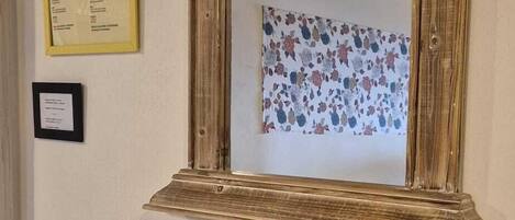 A mirror with a wooden frame, a small table with a vase of reeds, and framed informational plaques on the wall.
