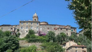 A historic building with a bell tower, surrounded by lush greenery and other residential structures. - La Rocca - casa con terrazza vista mare in borgo medievale (Camaiore)