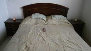 A bed with a beige quilt and two pillows, flanked by two wooden nightstands with clocks. - Servicio de Hotel (Bogotá)