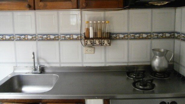 A kitchen with a stainless steel sink, a gas stove, and wooden cabinets. - Servicio de Hotel (Bogotá)