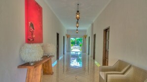 A hallway with a wooden bench, a red artwork, a wicker sofa, and a view of the outdoors.