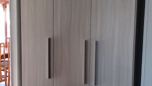 Ein großer Kleiderschrank mit zwei Türen und einem Griff, ein Holzboden und ein teilweiser Blick auf einen Essbereich mit Tisch und Stühlen.