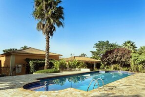 A swimming pool with a stone deck, palm trees, and a building with a tiled roof.