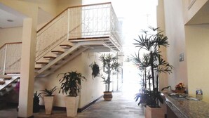 Eine großzügige Lobby mit einer zentralen Treppe, Zimmerpflanzen und einem Empfangsbereich.