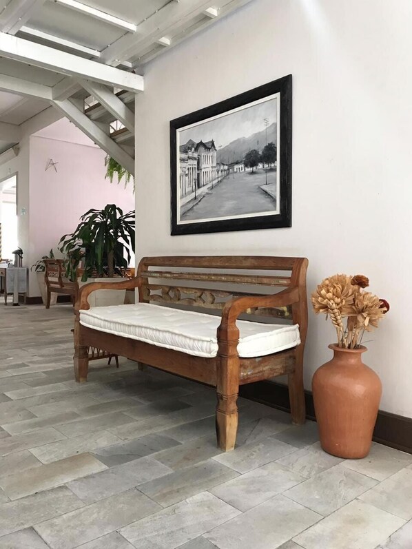 A wooden bench with a mattress, a framed black and white photograph on the wall, and a terracotta vase with dried flowers.