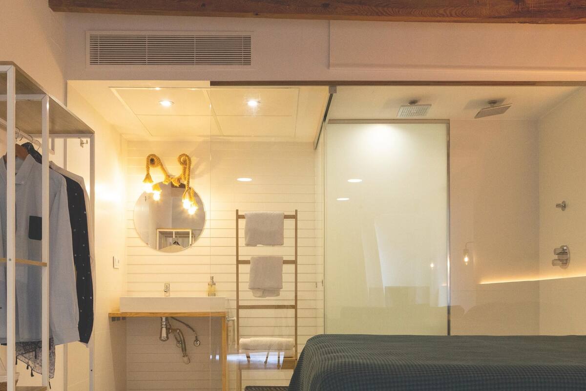 Un dormitorio con cama, armario, espejo y baño con ducha y lavamanos.