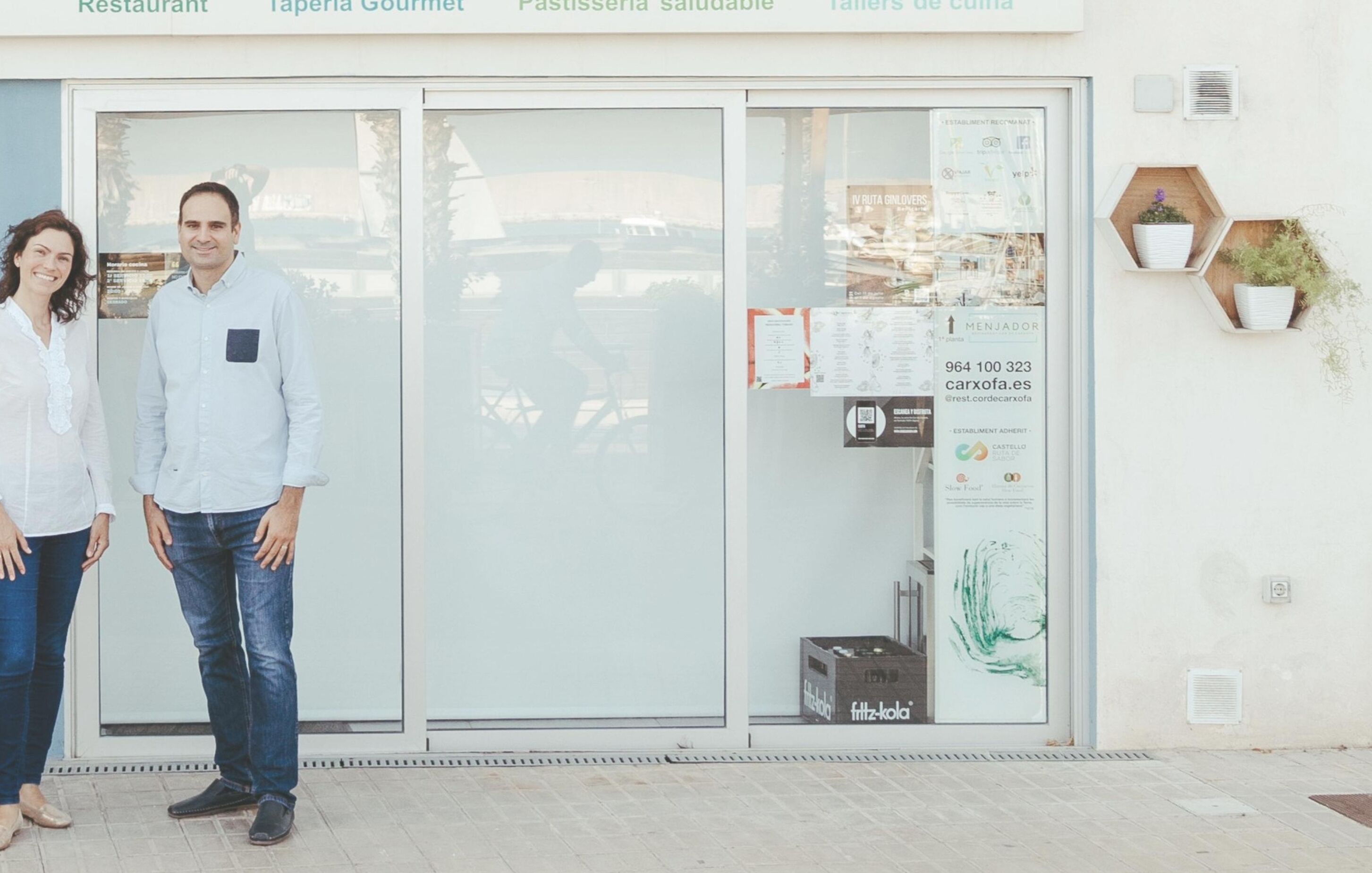 Fachada con puerta de vidrio, un cartel de menú y un pequeño arreglo de plantas en la pared.