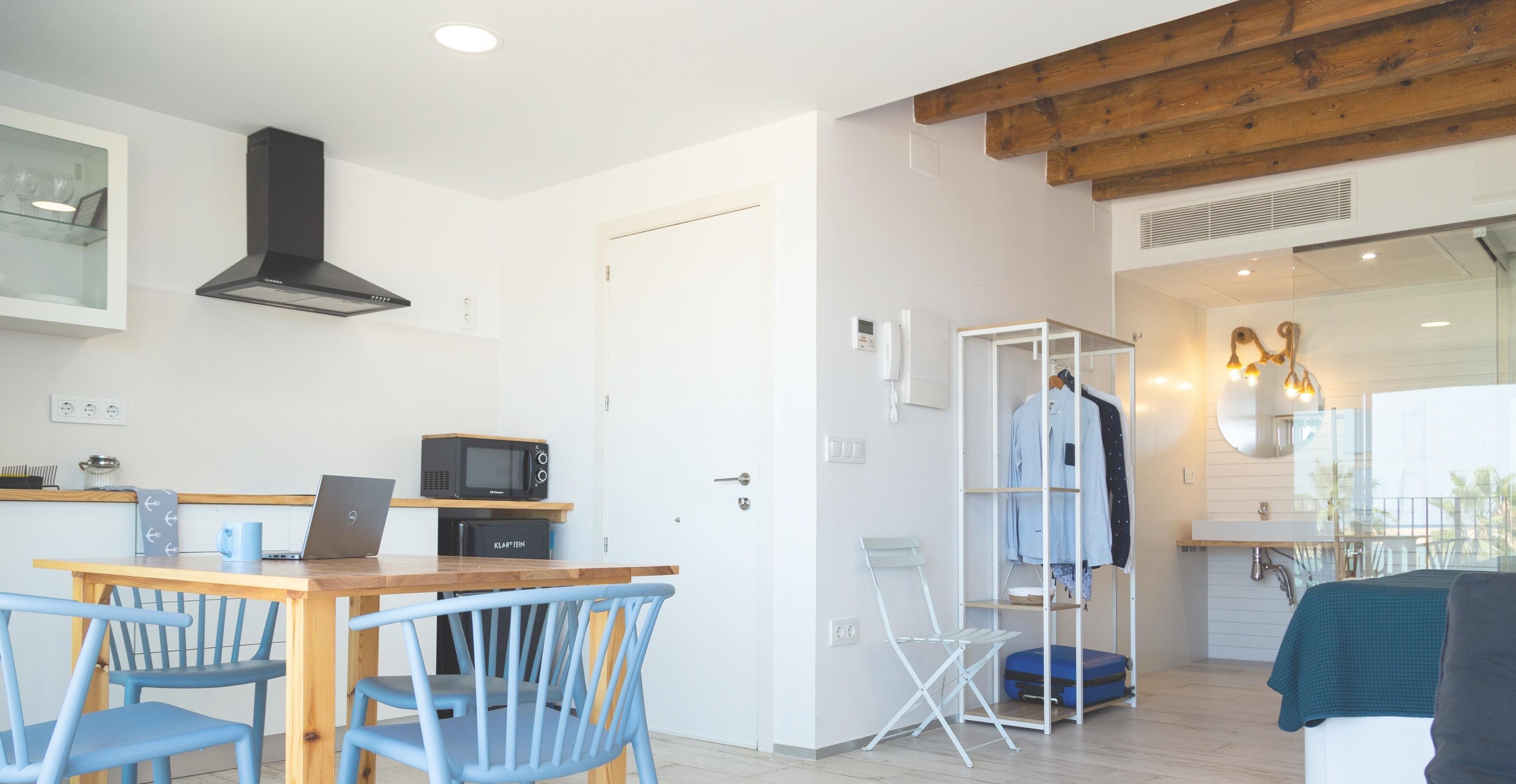 Een moderne keuken met een houten tafel, blauwe stoelen, een magnetron en een laptop.
