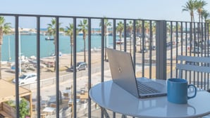 Ein Laptop auf einem Balkontisch mit Blick auf einen Hafen und Palmen.