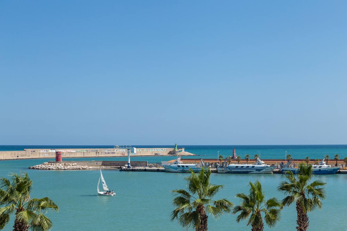 Un puerto deportivo con barcos amarrados, un faro y un cielo azul despejado.