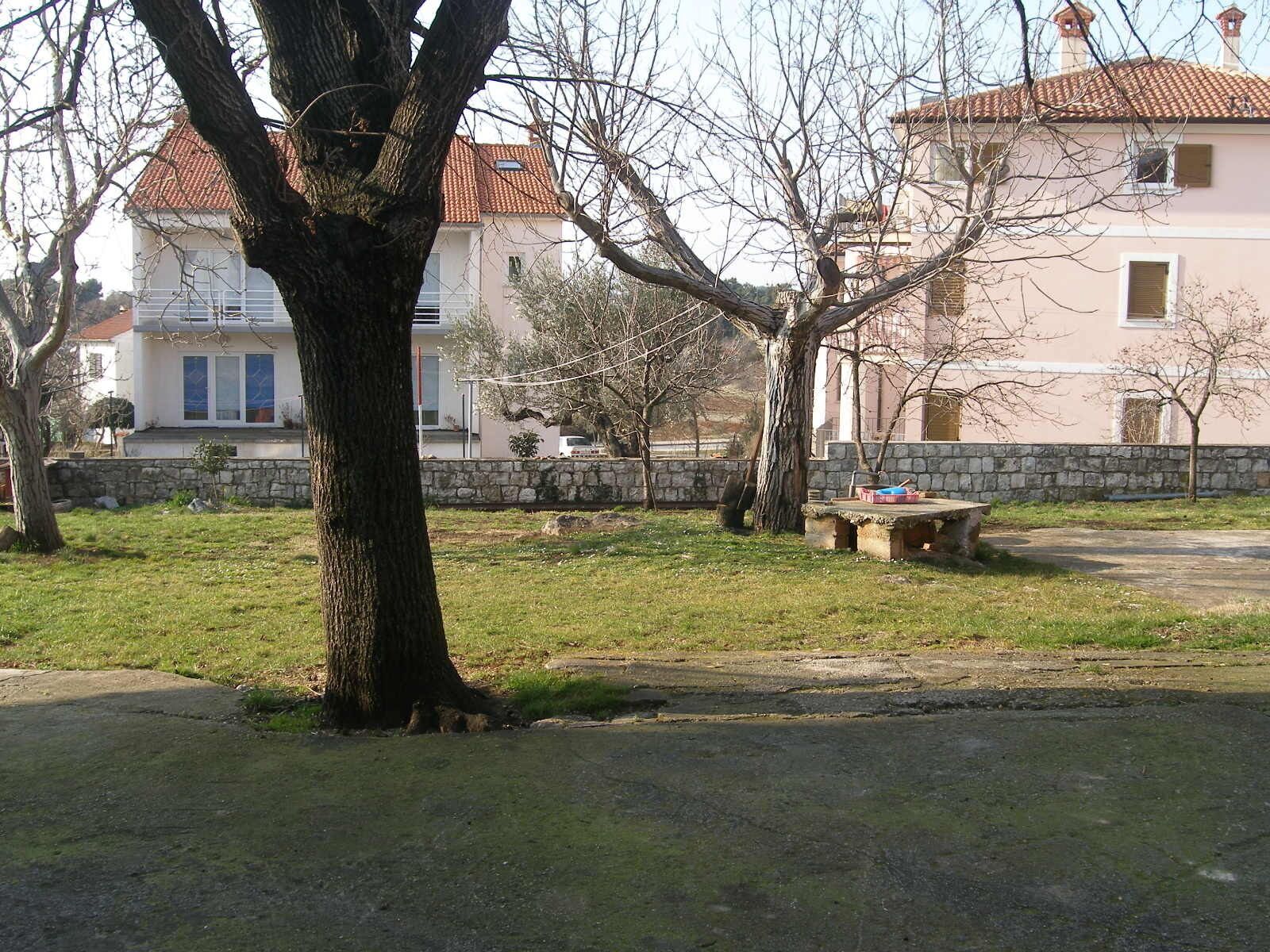 A park with a stone bench, trees, and a building with a red-tiled roof in the background.