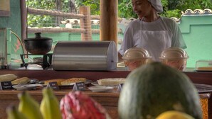 A food stall with various dishes displayed, a cooking stove, and a person in the background. - Pousada Pé na Estrada (Porto Seguro)