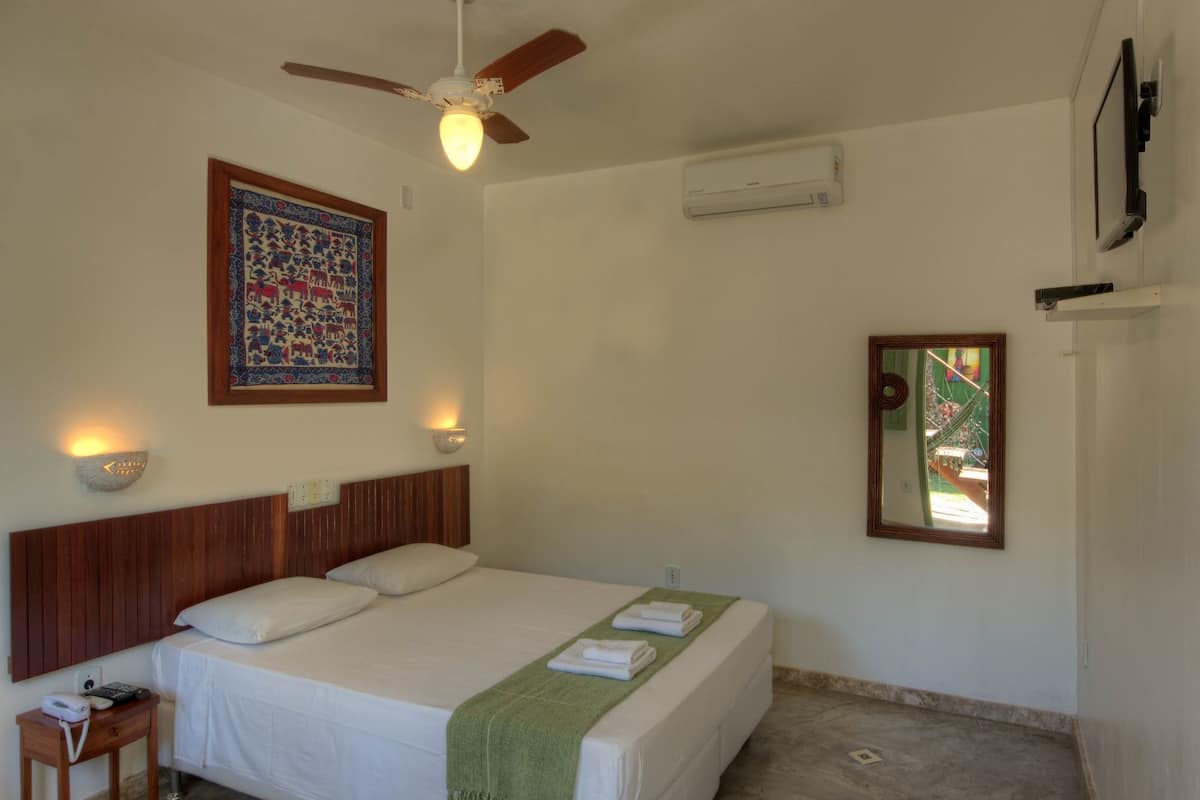 Ein Hotelzimmer mit einem Bett, einem Nachttisch, einem Deckenventilator, einem an der Wand montierten Fernseher und einem gerahmten Bild.