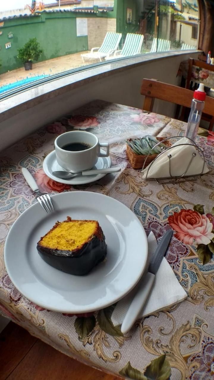 Ein Tisch mit einer blumigen Tischdecke, ein Teller mit Kuchenstück, eine Tasse Kaffee und eine kleine Handtasche.
