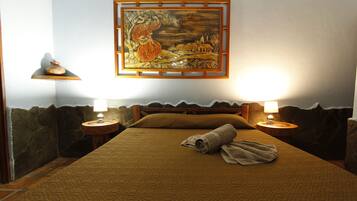 Quarto de hotel com cama, duas luminárias de cabeceira, um quadro na parede e parede de pedra.