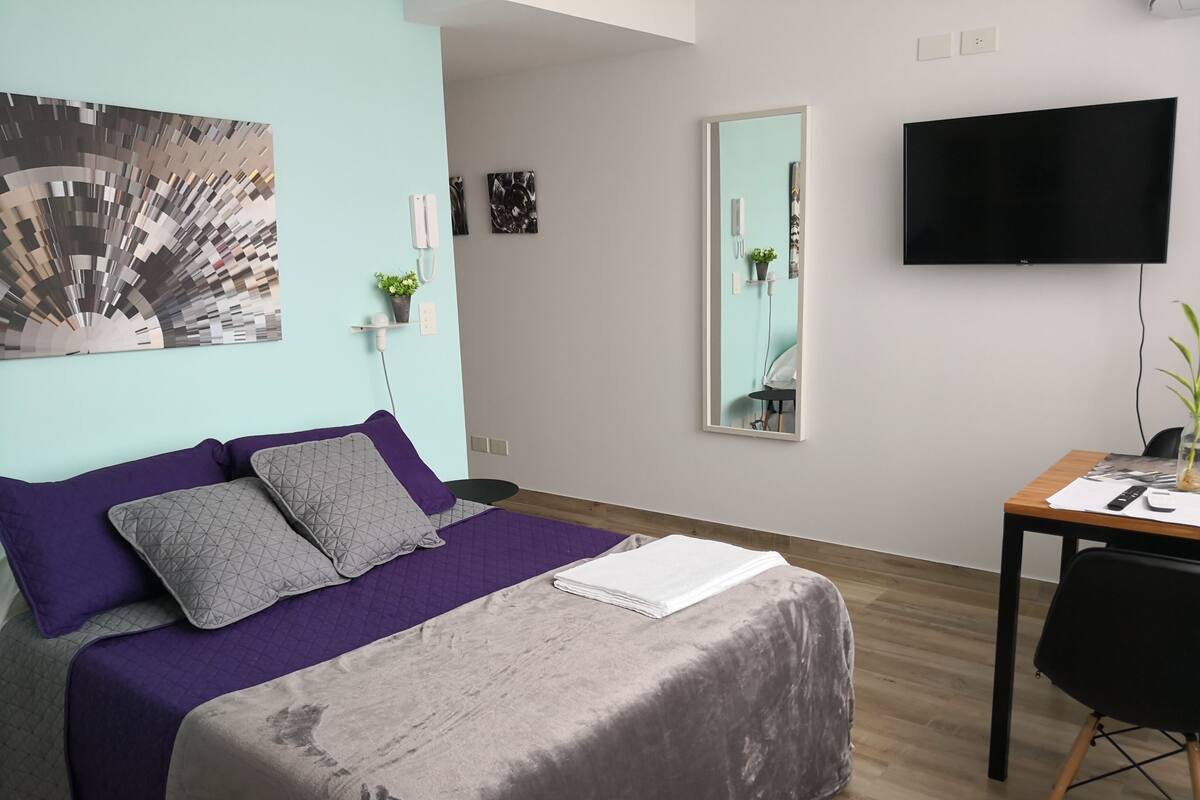 Ein modernes Schlafzimmer mit Bett, Schreibtisch, Stuhl, Fernseher und Spiegel.
