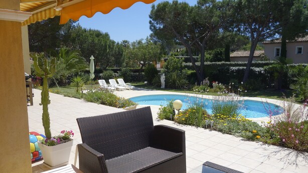 Eine Terrasse mit Korbmöbeln, einem Pool und üppiger Bepflanzung.