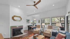 A spacious living room with a fireplace, a ceiling fan, and large windows offering a view of the outdoors. - Rare 3 Bedrm 2 Bath corner unit with unobstructed Spectacular Mountain Views (Tucson)