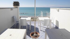 A terrace with a blue umbrella, white chairs, and a table overlooking the sea.