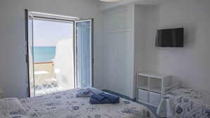 A bedroom with a bed, a TV, a wardrobe, and a balcony with a view of the sea.