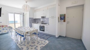 A compact kitchen with white cabinets, a dining table with chairs, and a view of the sea through a sliding door.