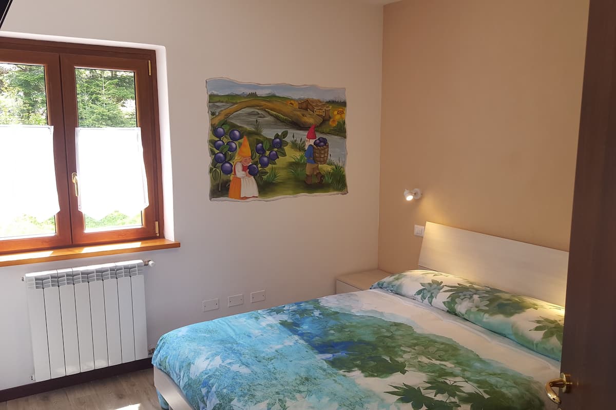 A bedroom with a bed, a radiator, a window, and a wall painting.