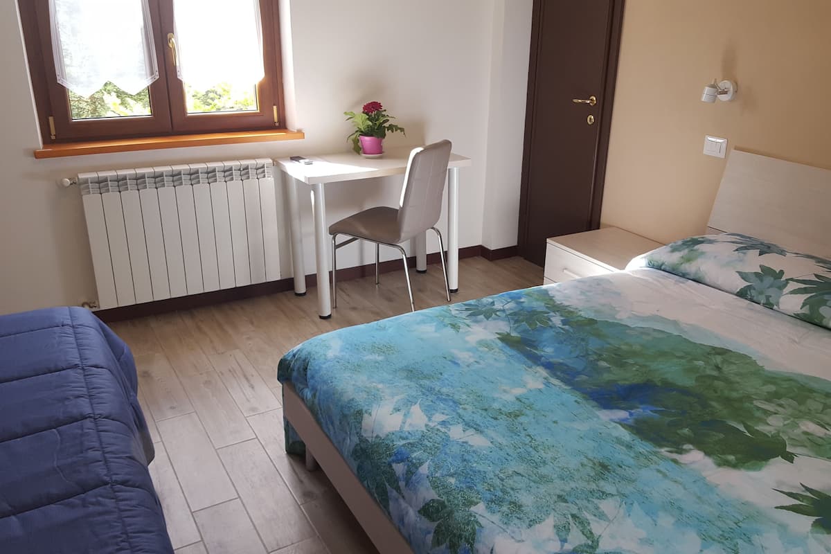 A bedroom with a bed, a desk, a chair, a radiator, and a window.