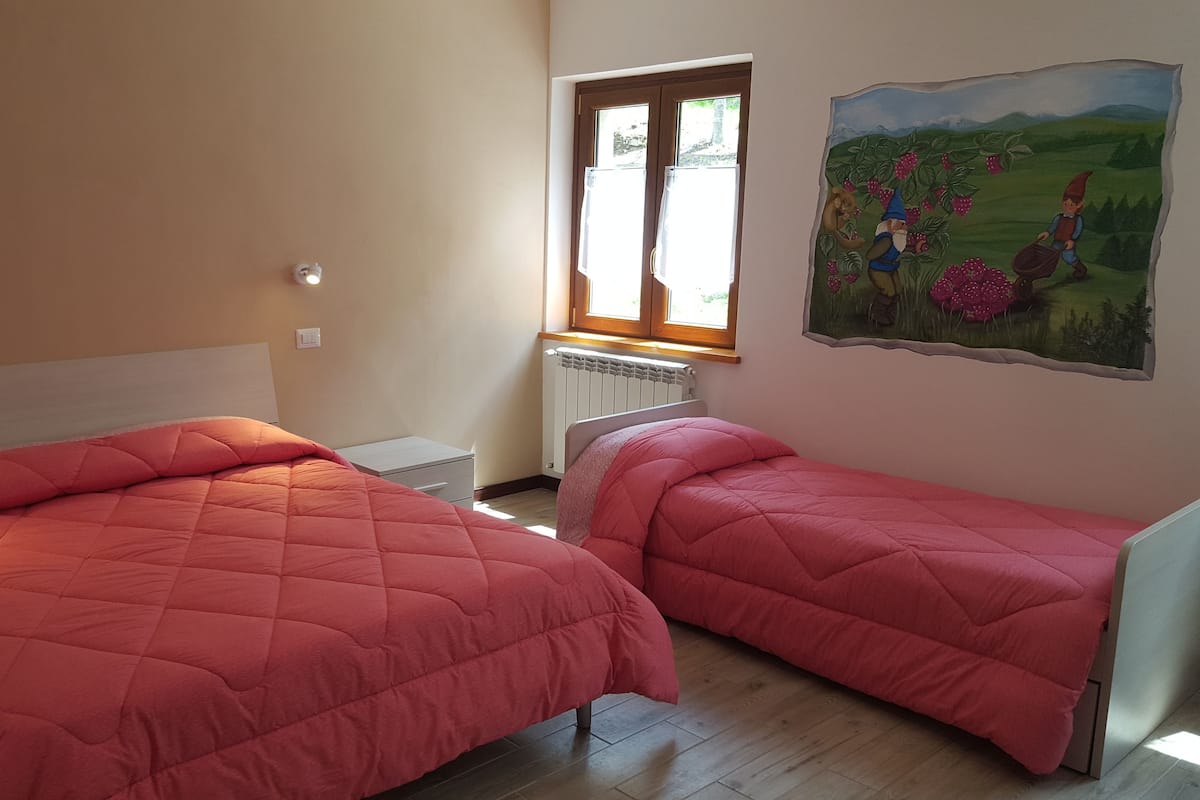 A bedroom with two beds, a window, a radiator, and a painting on the wall.