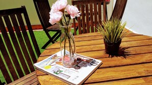 A wooden table with a newspaper, a vase with pink flowers, and a potted plant. - COLLECTION Bed & Breakfast, Centro Alicante I Cocina & Terraza - Jardín  (Alicante)