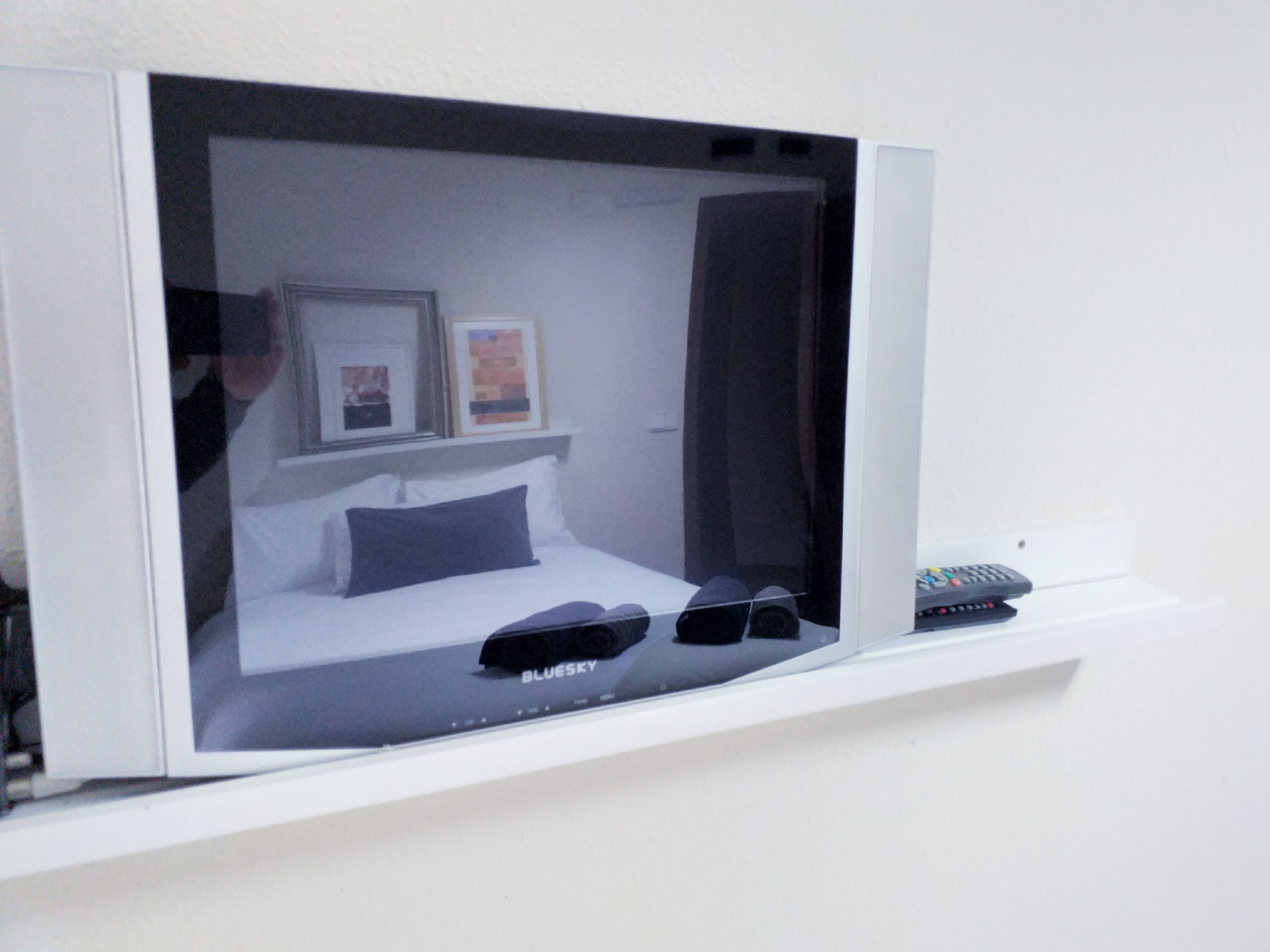 Habitación de hotel con cama, un par de zapatos, control remoto y cuadros en la pared.