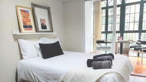 A neatly made bed with white linens and a black pillow, a pair of towels, and two framed artworks on the wall. - COLLECTION Bed & Breakfast, Centro Alicante I Cocina & Terraza - Jardín  (Alicante)