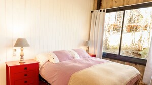 Et soveværelse med en seng, et rødt natbord, en lampe og et vindue med gardiner.
