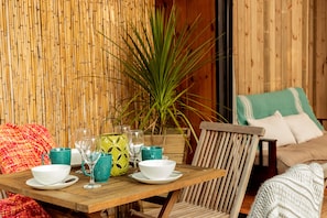 A wooden dining table with white and green bowls, glasses, and a green vase. A chair with a striped cushion is visible. - Yacu Beach (José Ignacio)