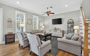 A living room with a sofa set, a coffee table, a TV, and a staircase. - Blue Cabana -Close To Red Fish and Beach, Pool, 3 Bikes (Santa Rosa Beach)