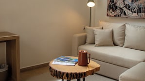 Una habitación con un sofá, una mesita redonda con un libro y una taza, una lámpara de pie, y un cuadro abstracto grande en la pared.