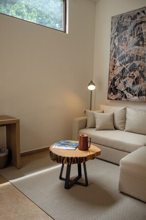 A room with a sofa, a small round table with a book and a mug, a floor lamp, and a large abstract painting on the wall. - Hotel Tabáa Oaxaca (Oaxaca)