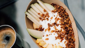 Un tazón de comida con rodajas de manzana, yogur y granola sobre una mesa.
