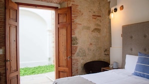 Un dormitorio con cama, mesita de noche, lámpara y vista a un patio.